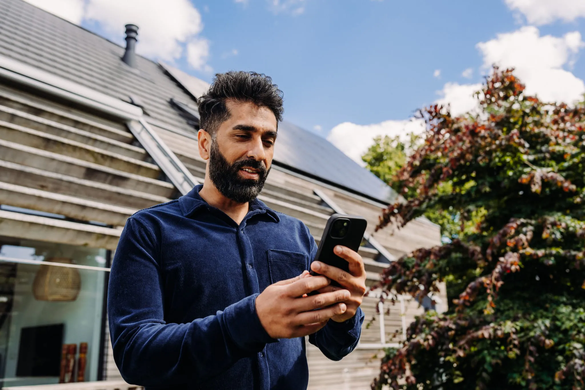 Une personne consulte l'app Chargee devant sa maison équipée de panneaux solaires